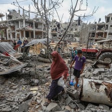 Woman and boy walk through street filled with rubble and lined by bombed-out apartment blocs