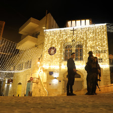 Soldiers carrying weapons stand beside an illuminated building 