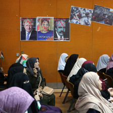 A group of people sit beneath three posters depicting British PM Boris Johnson, British minister Priti Patel and Arnold Balfour, who penned the Balfour declaration, giving away Palestine