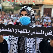 A woman in a face mask holds up a banner in Arabic