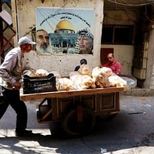 A man pushes a cart with bread in front of a poster depicting the al-Aqsa mosque in Jerusalem