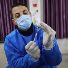 Man wearing mask and gloves holds a syringe 