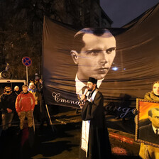 People watch a man in religious garb speak in front of a huge portrait of Stepan Bandera