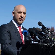 A besuited man speaks into several microphones