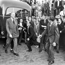 A man in a suit walks through an angry crowd not quite held back by uniformed police officers