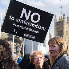 Two women can be seen beside a placard bearing the words No to antisemism enough is enough
