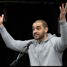 A man raises his arms while speaking into a microphone