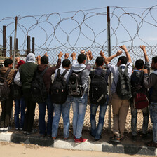 Palestinian students look through barbed wire at power plant