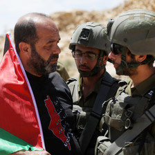 A man with a Palestinian flag confronts two soldiers