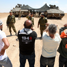 A group of young men confronts soldiers standing beside tanks 