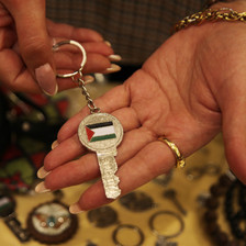 A woman holds a key bearing the Palestinian flag in her hand