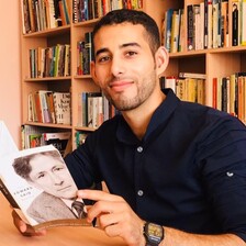Mosab Abu Toha sits at a table in the Edward Said Library holding a book