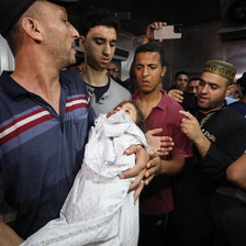 A man surrounded by other people carries the shrouded body of a child
