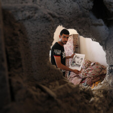 A man holds a drawing through a hole in a wall caused by the Israeli bombing campaign in early August