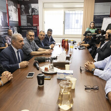 Around a dozen people sit at and stand around conference table