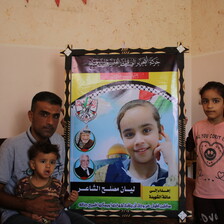Man and two children beside a large photograph of a girl