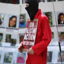 A masked man with a poster stands in front of pictures of children slain in Gaza