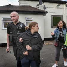 A police officer takes away a handcuffed woman, turning to speak to two others behind her