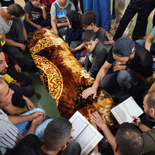 Men and boys sit beside a body covered by fabric. 
