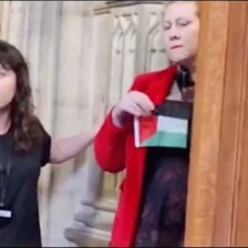 One woman places her hand on the plinth of a statue while another woman holds a small flag