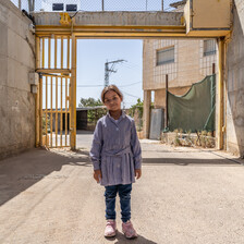 A girl stands before a yellow metal gate