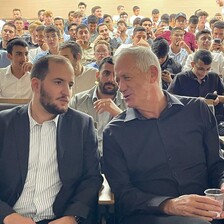 Two men sitting in an audience lean towards one another