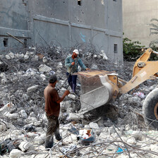 Two Palestinian laborers standing on a pile of rubble, next to a bulldozer