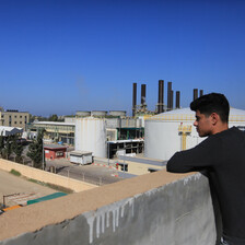 Man stands beside a wall that overlooks a power plant 