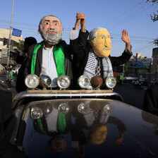 Two men wearing masks depicting Ismail Haniyeh and Mahmoud Abbas wave from a black car