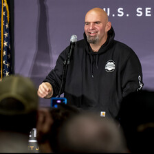 Man wearing a hoodie stands beside flag with stars and stripes