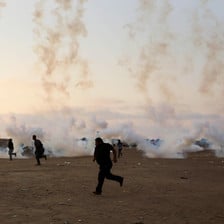 Clouds of tear gas smoke rise from canisters on the ground as a group of Palestinian men run for safety