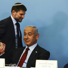 Bezalel Smotrich grasps a seated Benjamin Netanyahu's hand while they both smirk