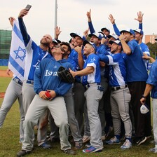 Members of the Israeli baseball team pose for selfies beside a flag 