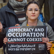 A woman holds a sign reading democracy and occupation cannot coexist