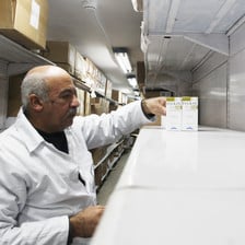 A pharmacist wearing a white coat stands next to a shelf with very few medicines in a Gaza warehouse 