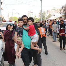 A man holds two young boys in his arms as people gather in street