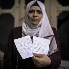 Woman wearing a white headscarf holds two pieces of paper in one hand