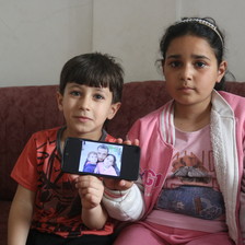 A boy and a girl sit on a sofa holding a mobile phone 