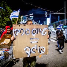 A man holds a hand-written sign in Hebrew