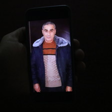 A cell phone photograph depicting Amin Warda in a jacket surrounded by a dark background.
