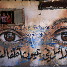 A mural in Gaza city depicts a closeup of realistic eyes as children peek out from a window embedded in the mural