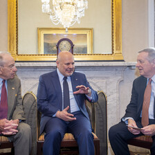 Grassley, Khan and Durbin sit in chairs in front of mirror reflecting chandelier