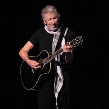 The musician Roger Waters wears a black and white checkered scarf while playing guitar onstage