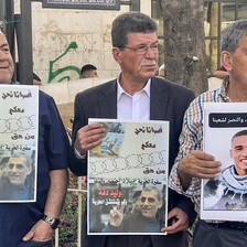 Three men hold up protest signs with images depicting Palestinian prisoners and also Egyptian police conscript Muhammad Salah