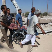 Four men assist a woman in a wheelchair navigate the rubble following an Israeli attack