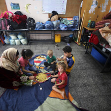 A woman and four children sit on rugs on a floor 