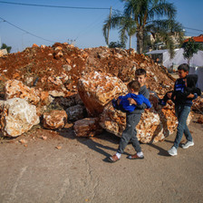 Palestinian children walk by a giant mound of red dirt and rocks that has been erected by the Israeli army