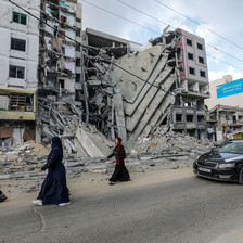 Four people walk past a building badly damaged by an Israeli air strike 