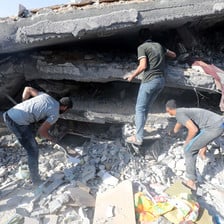 Three men search in the remains of a building that has been badly damaged by an Israeli airstrike