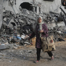 A woman with a shopping bag walks past a building that has been bombed in the Khan Younis area of Gaza 